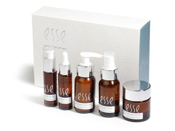 festive_gift_pack A skincare gift pack featuring five items in brown bottles with white labels that read "esse." The set includes a serum, an extract oil, a gentle cleanser, a sensitive toner, and a rich moisturizer, all placed in front of a white patterned box with the "esse" logo.