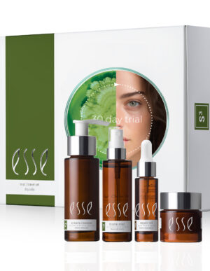 An image of the "Esse Dry Skin Trial / Travel Set" skincare collection. The set includes four brown bottles of various sizes and shapes labeled "cream cleanser," "biome mist," "repair oil," and "rich moisturizer." The packaging features a partial face and green plant.