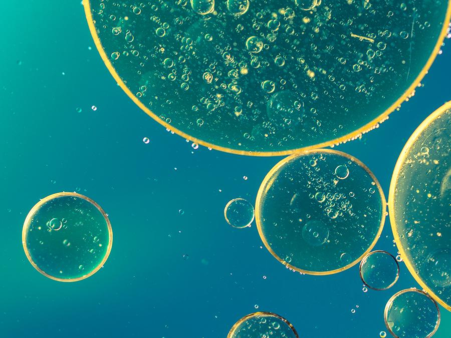 Close-up of several translucent bubbles of various sizes floating in a teal liquid. Each bubble contains numerous tiny air pockets, creating a dotted texture. The light creates a slight glow around the edges of the bubbles, giving a whimsical effect.