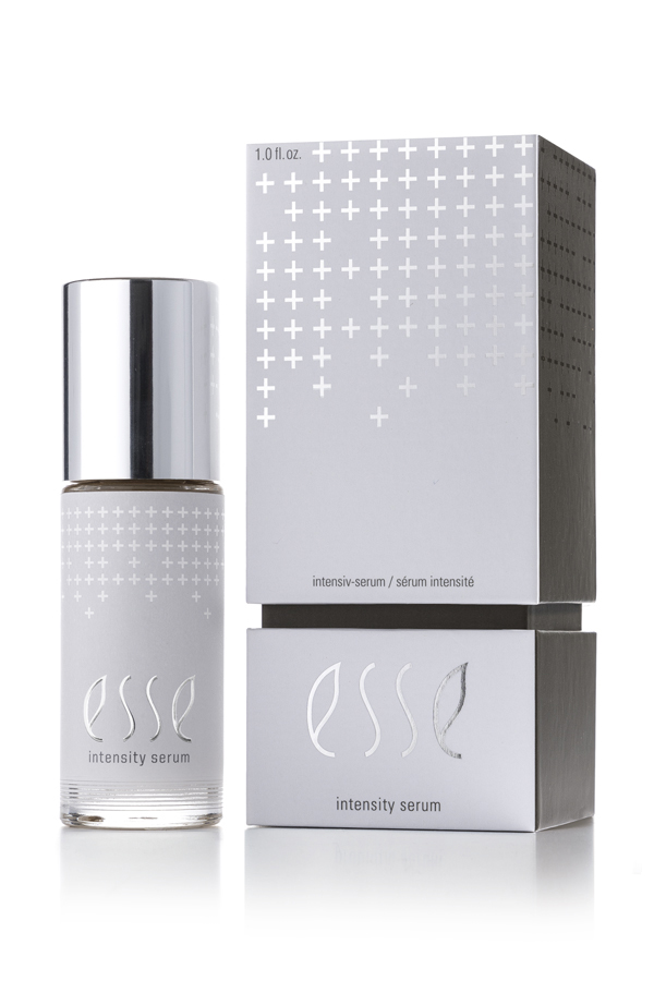 A bottle of Esse Intensity Serum with a shiny silver cap sits beside its matching silver and white box, both displaying minimalist text and a pattern of white plus signs.