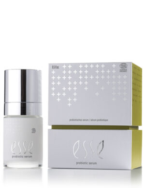 A bottle of Esse Probiotic Serum with a shiny silver cap sits beside its white-and-green box, which features silver cross patterns along with the product name and details.