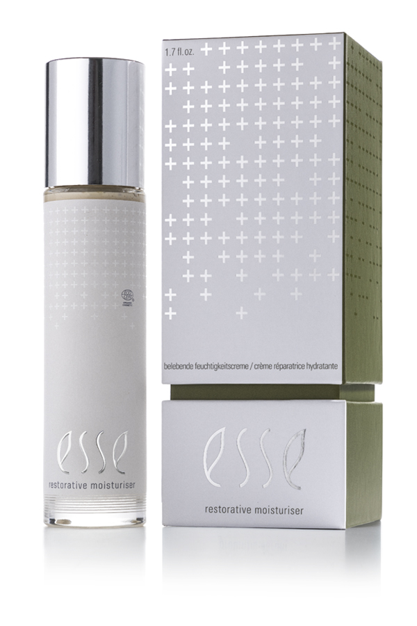 The Esse Restorative Moisturiser, featuring a silver cap, is displayed beside its box. Both have a minimalist design with white crosses and silver text on muted green and gray backgrounds.