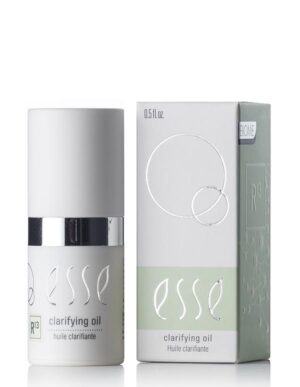The image features a bottle of Esse Clarifying Oil along with its packaging. The cylindrical bottle is adorned with a white cap and a metallic silver band. The light green and white box showcases the product name and various branding elements. The bottle has a capacity of 0.5 fl oz.