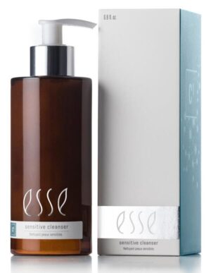 A bottle labeled "Esse Sensitive Cleanser" with a pump dispenser and brown in color is positioned next to a silver and white box that features the same branding. The bottle's label showcases white text, while the box has a metallic strip near the bottom providing product information.