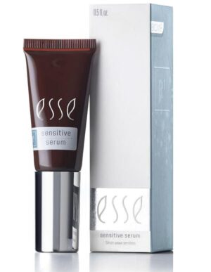 A sleek tube of Esse Sensitive Serum, in a sophisticated dark color, features a metallic silver cap and stands beside its light grey packaging box adorned with subtle decorative patterns. Both the box and the tube display the product name and a volume of 0.5 fl oz.