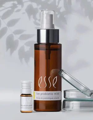 Two brown bottles of Import placeholder for 56090 are on a light surface, accompanied by a clear petri dish and leafy shadows in the background.