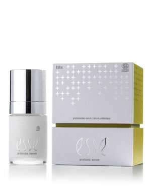 A bottle of Esse Probiotic Serum with a shiny silver cap stands beside its white box, featuring metallic silver cross designs and gold sides. The label displays the product name, “Esse Probiotic Serum.”.